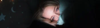 Tipy pro lepší spánek: žena unavená spí v posteli, osvícená světlem mobilního telefonu.